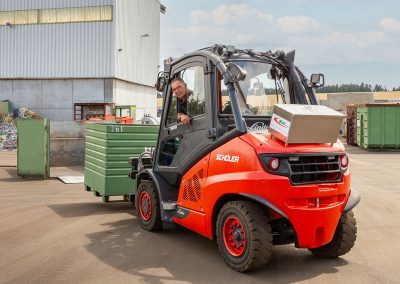 Gabelstapler, transportiert auf der Gabel gerade einen grünen Metallbehälter